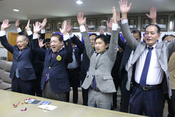 開催地決定に万歳し、笑顔を見せる桑江市長(写真手前左から2人目)=9日、沖縄市役所