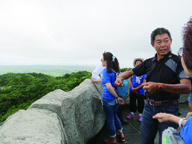 台湾移民が入植した名蔵地区について、一行に説明する王滝さん=21日午前、バンナ公園