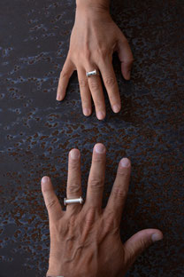 Photographie de deux mains se rejoignant portant chacune une bague en argent en forme de U avec tube