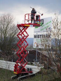 Scheren-Raupenbühne mit Arbeiter, der ein Schild reinigt