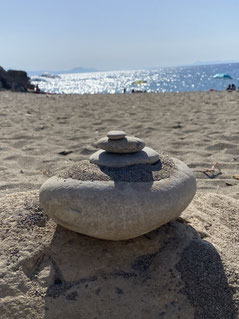 Auf dem Bild ist ein kleines Steinmännchen am Sandstrand am Meer zu sehen.