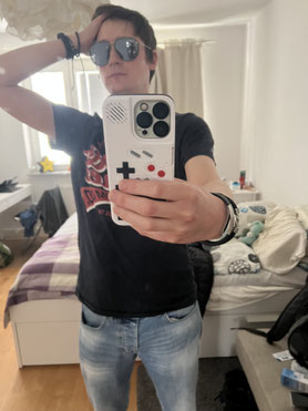 Picture of website owner wearing sunglasses, various bling and showing off a Gameboy phone case.