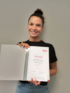 Teilnehmerin mit schwarzem Shirt hält Zeugnis vor grauem Hintergrund