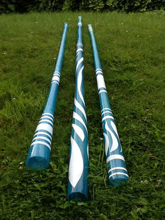 Three Fibreglass Didgeridoos in blue, on a green lawn. Decoration made of curved and cross lines in white.