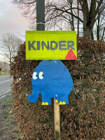 Straßenschild als Hinweis vor der Schule. Der blaue Elefant aus der Sendung mit der Maus mit einem Schild.
