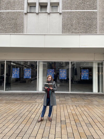 Zukunftsforscherin Janine Seitz mit dem neuen Buch von Hartmut Rosa vor dem noch leerstehenden Sportscheck in Wiesbaden