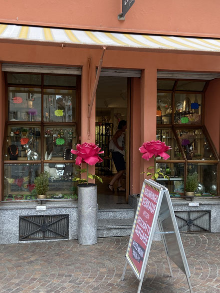 Ladenfront rotes Altstadt Haus in Konstanz am Bodensee mit gelb gestreifter Markise und zwei überdimensionalen Kunstblumen links und rechts neben der Eingangstür. Ein Schild Räumungsverkauf wegen Geschäftsaufgabe steht vor dem Laden. Schmuck Schaufenster