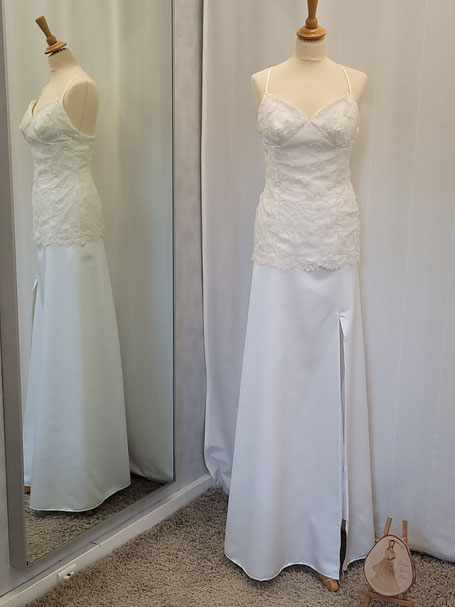 Robe de mariée unique, ajustée au niveau du buste affinant la silhouette, recouvert de dentelle, bas légèrement évasé. Couleur blanc soie