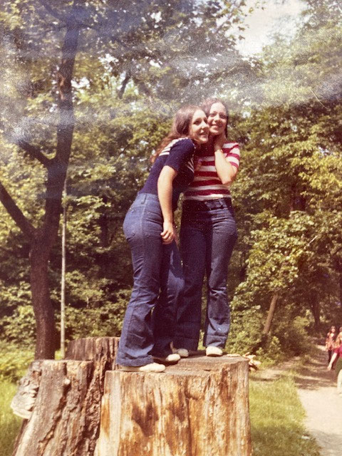 Das Bild aus dem Jahr 1974 zeigt auf einem Baumstamm stehend Kundin Sissi rechts - sie trägt blaue WRANGLER Jeans und links im Bild ist ihre Freundin Gabi, sie trägt blaue Levis Jeans