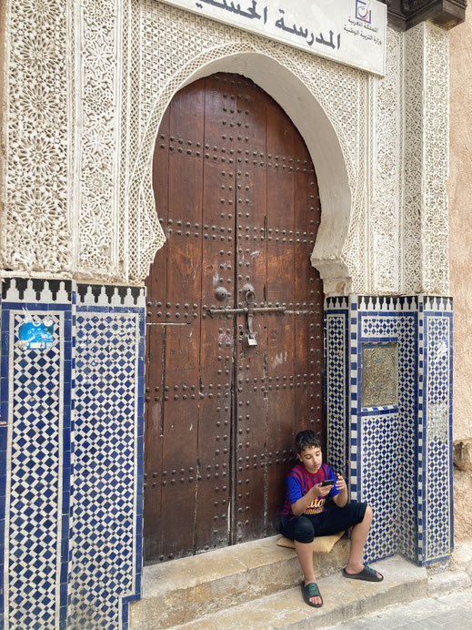 Ein Junge sitzt auf einer Türschwelle mit maurischem Bogen in Fez, Marokko - Spurenwechsler