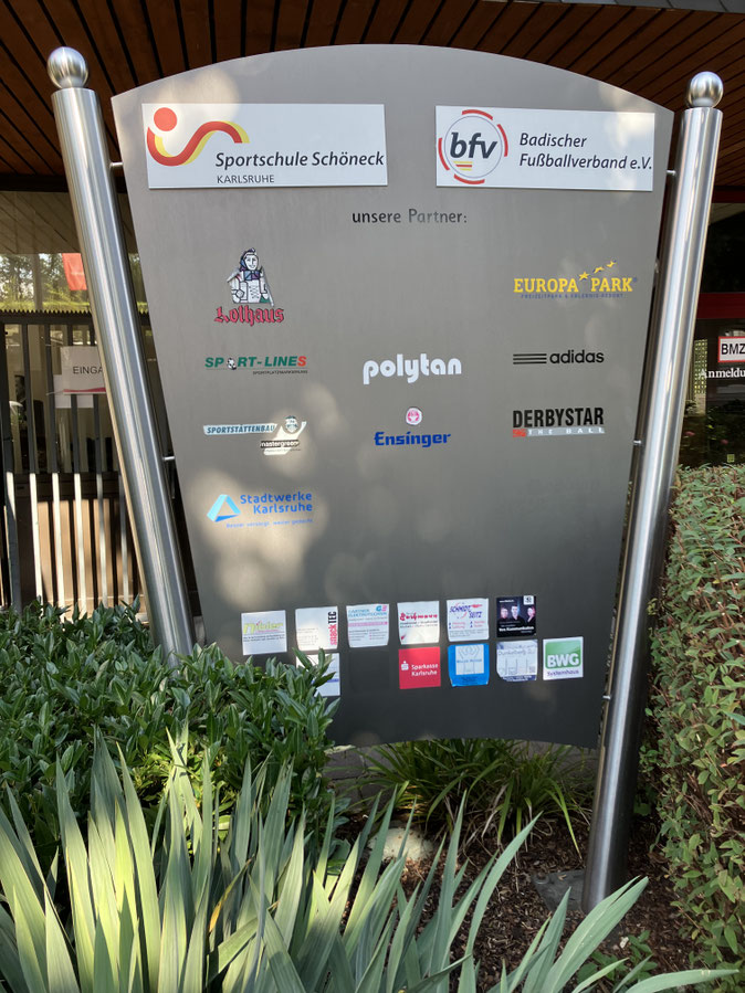シュポルトシューレ・シェーネック 門のそばに立っている看板、バーデンサッカー協会のほか、複数のスポンサー名が並ぶ