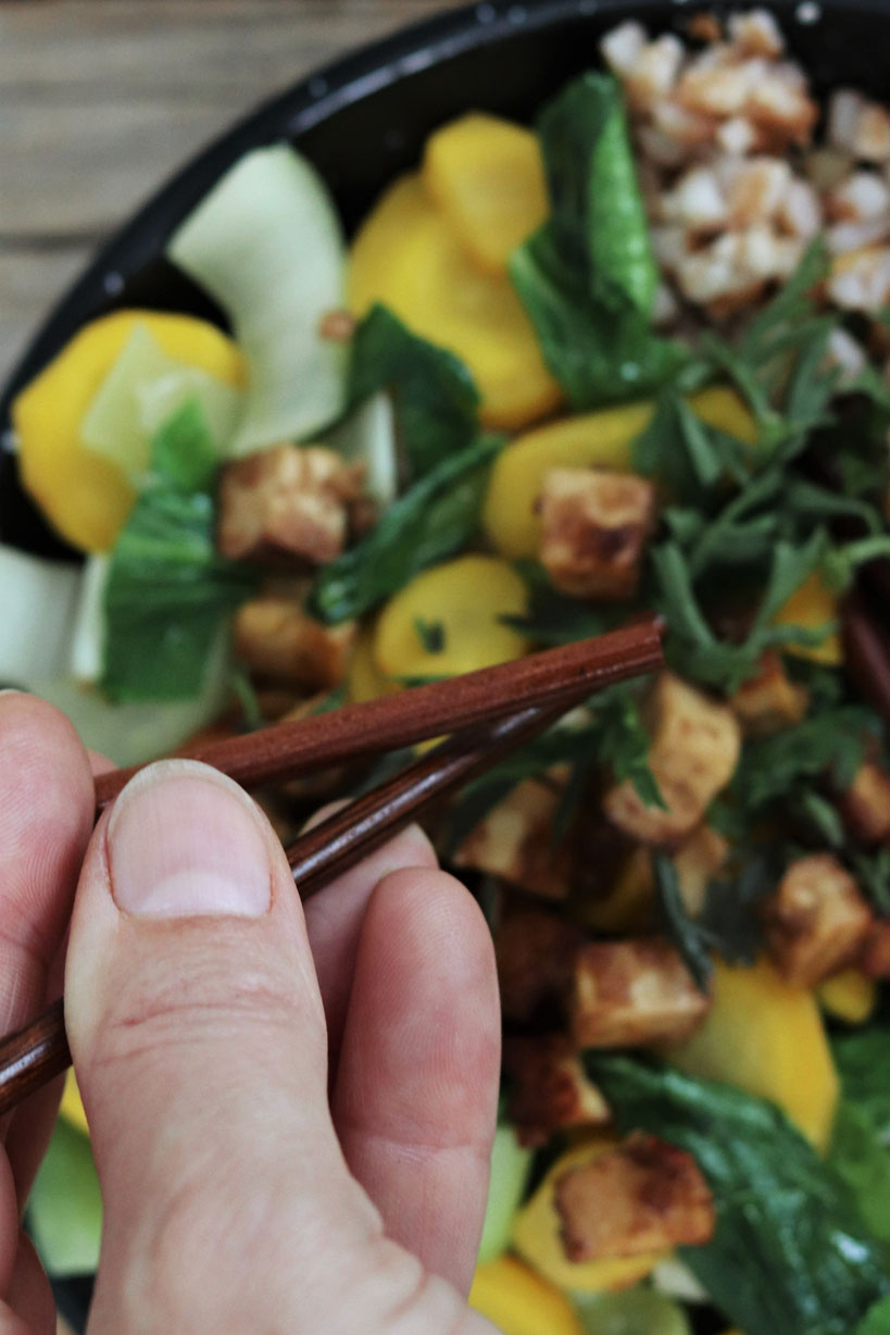 Pak Choi mit Karotten und Tofu werden mit Essstäbchen gegessen