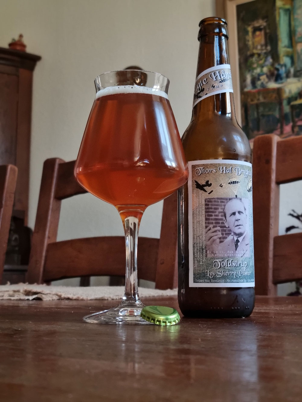 ‼️‼️NYHED ‼️‼️TOLDSTRUP‼️‼️  Toldstrup - Lys Sherry Pilsner   Opskrift nr. 22  -  den nyeste øl fra Thors Hal, er en hyldest til frihedskæmperen Toldstrup fra Assens. Født 30. juni 1915 og ved dåben fik han navnet Anton Ingersøn Jensen.  Han var uddannet hos toldvæsenet,  deraf han fik sit illegale navn "Toldstrup".  Denne øl er så fynsk den kan blive. Den er brygget på ren fynsk pilsnermalt fra Refsvindinge Malteri, humlen er Perle og den er tilsat en eksklusiv spansk 15 års sherry, som er modnet på egetræ.   Farven er dyb gylden, duften er præget af sød karmel, frugtig noter og man fornemmer en svag duft af sherry. Smagen er fyldig og aromatisk, humlens bitterhed træder frem og giver en læskende fornemmelse. Øllen er kraftigt og er i kategorien "stærk pilsner" på Alk. 6,2% Vol. Smagen bliver længe i munden og man fornemmer sherryens sødme, efterfulgt af egetræ fra sherry fade.  En stærk pilsner, der er en frihedskæmper værdig, en som Toldstrup.  Hans motto var "Ingen Kamp Uden Sejr"  Navnet "Toldstrup" er brugt med tilladelse fra Toldstrup Selskabet og familie.  Toldstrup selskabet fejre hans fødselsdag d. 30. juni 2024.