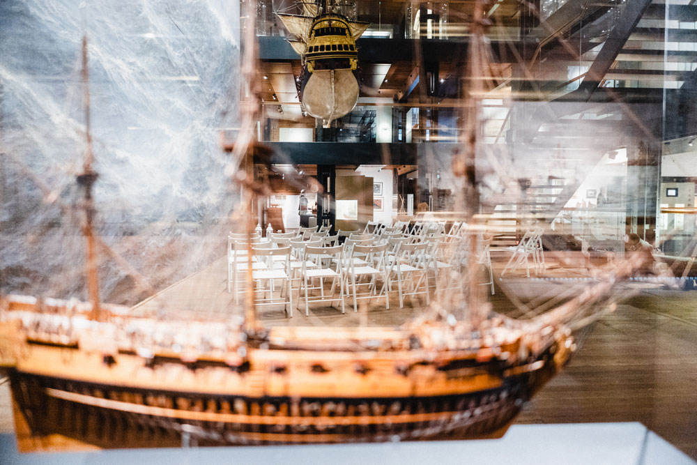 Im Maritim Museum vor einer Trauung. Das Foto ist durch Glas Fotografiert, im Vordergrund, verschwommen, erkennt man das Model eine Segelschiffes, im Hintergrund, scharf, erkennt man die Stühle für die Freie Trauung