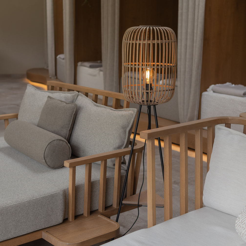 Gemütlicher Spa-Loungebereich mit hellen Polstermöbeln aus Holz, dekorativen Kissen und einer warm leuchtenden Stehlampe im natürlichen Design.