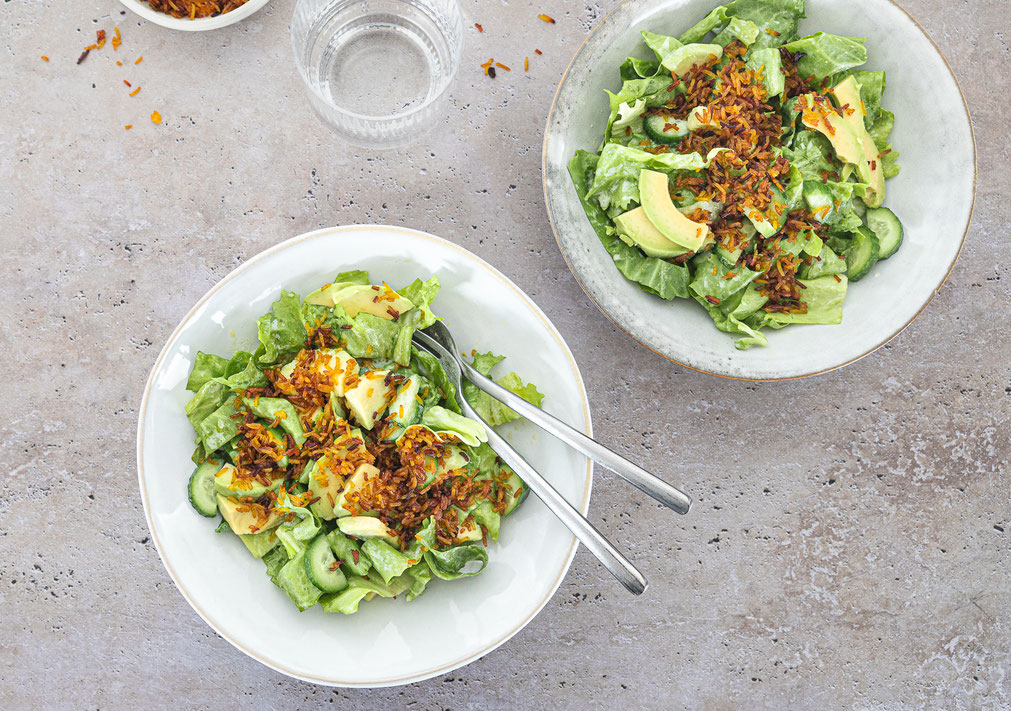 Knusprige Reis-Bowl mit Endiviensalat, Avocado und Gurke, serviert mit cremigem Dressing auf einem hellen Teller