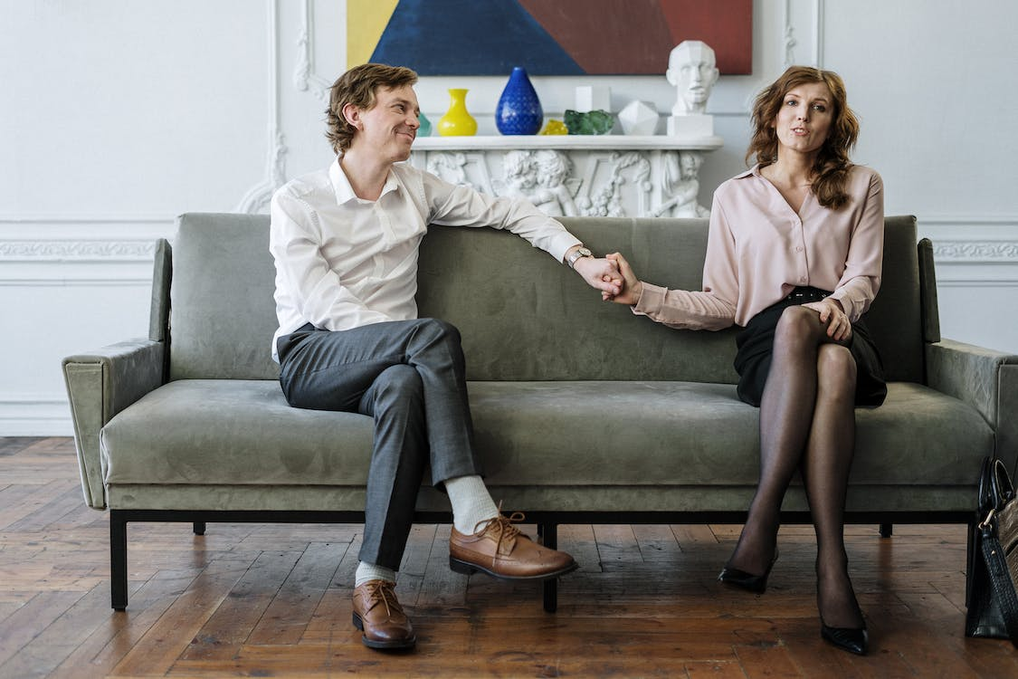 A couple holding hands while seated on a green couch