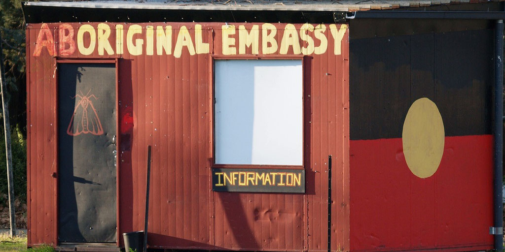 A small red building labeled "Aboriginal Embassy" features an information sign and the Aboriginal flag painted on the side.