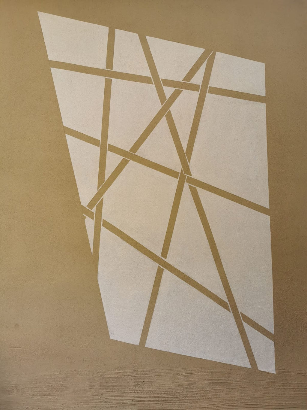 Geometrische Wandgestaltung mit Lehmfarbe in Lehmbraun und Creme, abstrakte Flächen mit schräg verlaufenden Linien im Innenbereich.