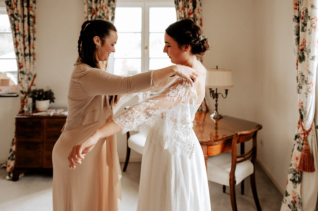 Die Trauzeugin hilft der Braut beim Getting Ready in das Brautkleid