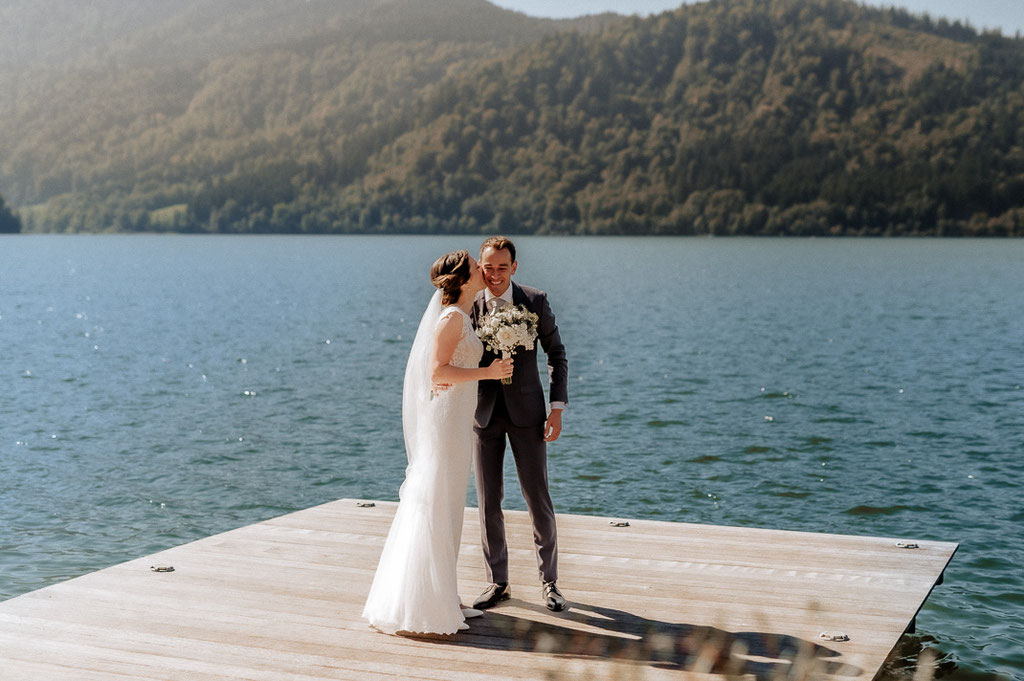 Hochzeitsfotografie Schliersee, die Braut küsst den Bräutigam auf die Wange. Sie stehen auf einem Steg am Schliersee.