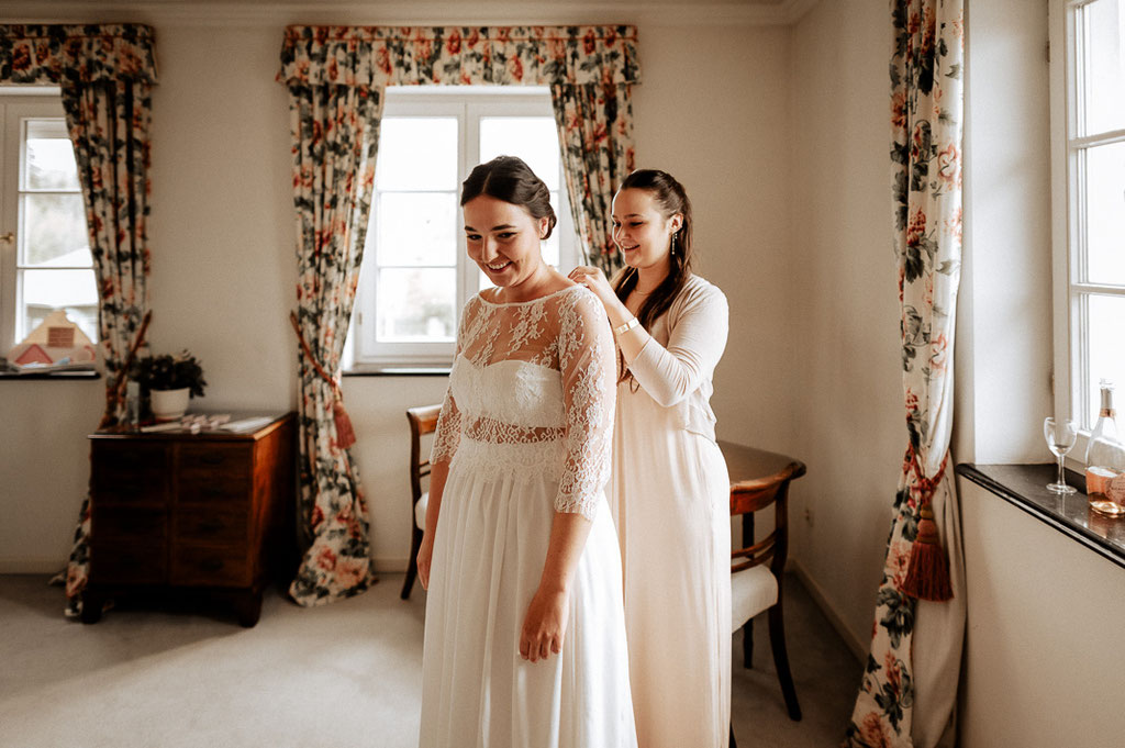 Die Trauzeugin hilft der Braut ihr Brautkleid zuzuknöpfen- ein Augenblick voller Vorfreude und Emotionen