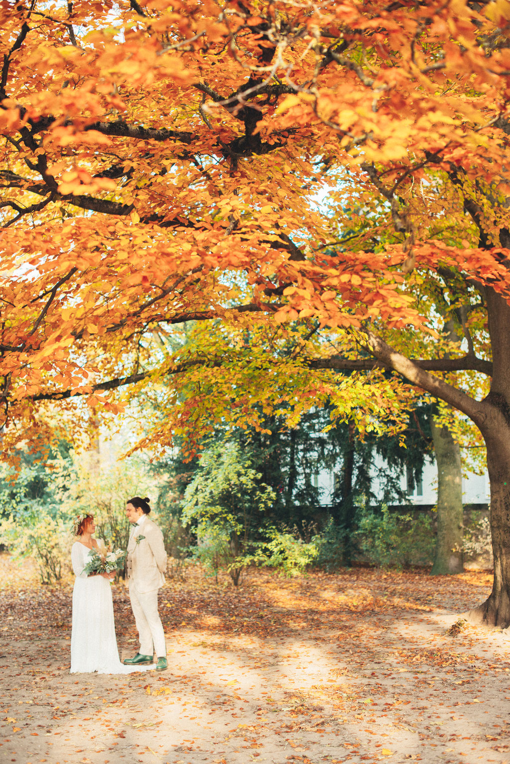 Professionelles Hochzeitsfoto von Braut und Bräutigam in herbstlicher Umgebung unter einem großen Baum.