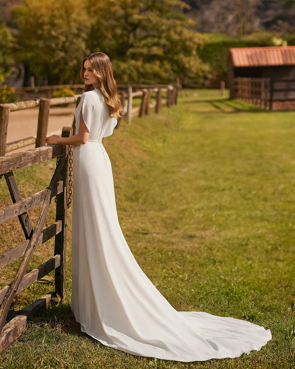Junge Frau trägt auf einer Pferdekoppel das Brautkleid Nariol aus der Alma Novia Kollektion 2026