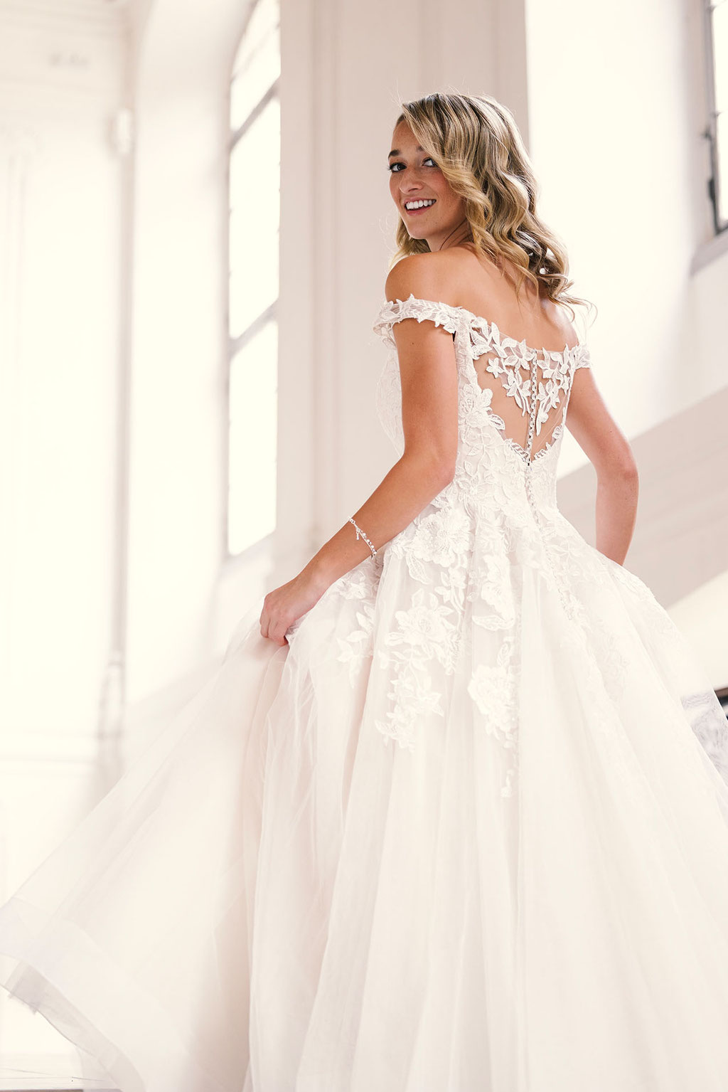 Junge Frau blickt seitlich nach hinten und trägt das Brautkleid Carlotta aus der Amo & Luv Kollektion