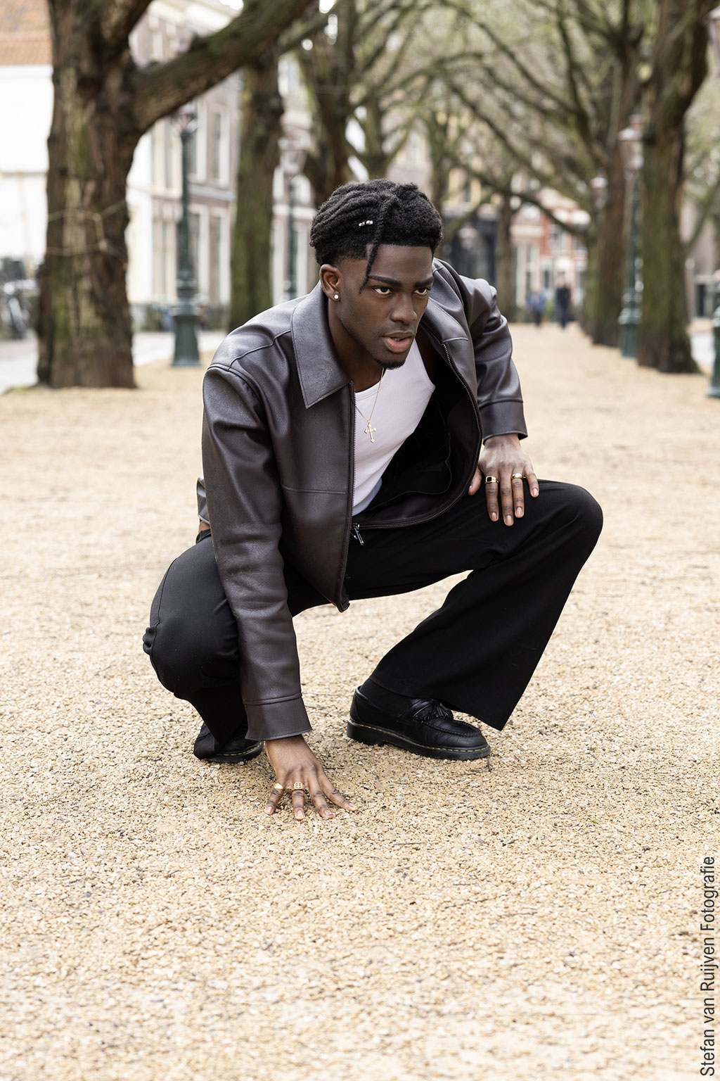Benjamin gefotografeerd in Leiden om zijn portfolio bij New Generation Models een update te geven. Hij draagt een aubergine leren jack, witte tanktop, zwarte broek en zwarte schoenen, Hij zit door zijn knieën. Gefotografeerd door Stefan van Ruijven 