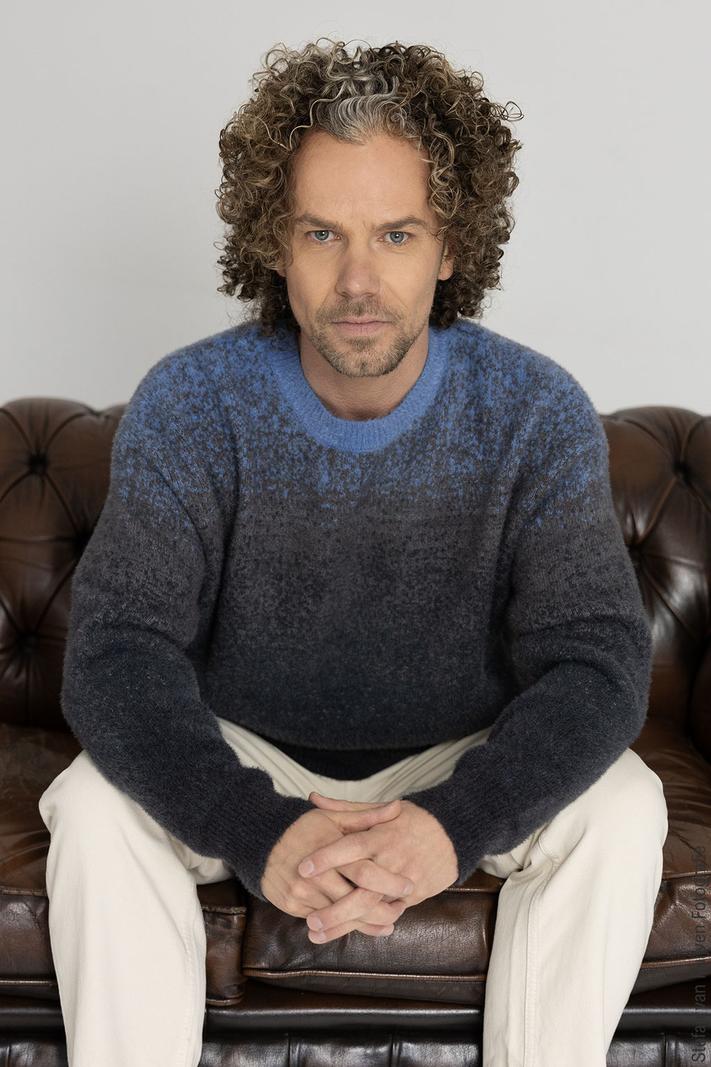 Stefan poseert op een bruine leren bank in Studio Duinlust. Portfolio maken tijdens de Fotoshoot Dag op vrijdag 27 februari 2026. Hij draagt een blauw met grijze trui, lichte broek en Nike sneakers in blauw/geel. Foto's gemaakt door Stefan van Ruijven 
