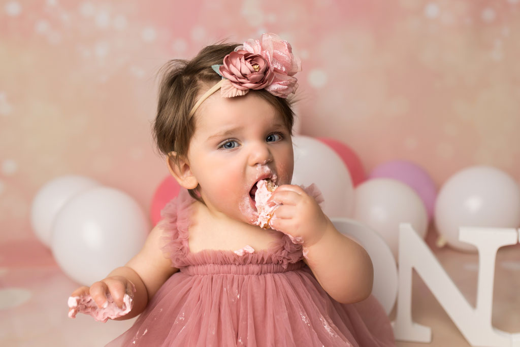 Kleines Mädchen isst genüsslich von der Geburtstagstorte beim Cake Smash Fotoshooting