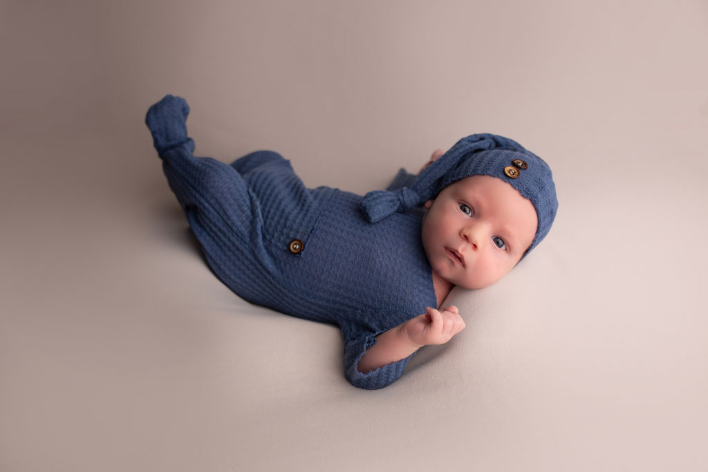 Neugeborenes in einem blauen Outfit auf einer neutralen Decke