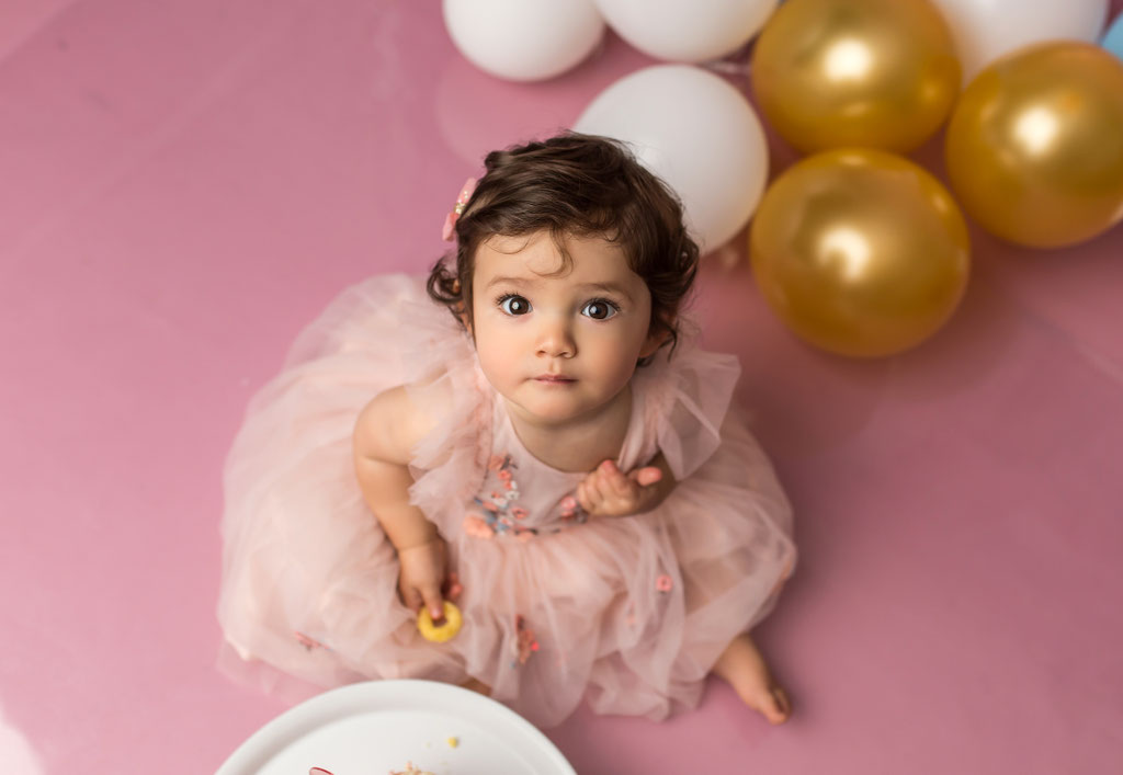 Kleines Mädchen mit Torte im Gesicht vor rosa Studio-Hintergrund