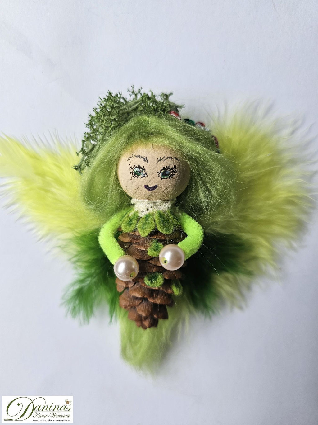 Waldfee Figur Tilia aus Fichtenzapfen, mit lindgrünen Haaren aus Wolle, gelb-grünen Federnflügeln, grünen Blättern aus Filz. Irisches Moos und Ziersteine als Haarschmuck