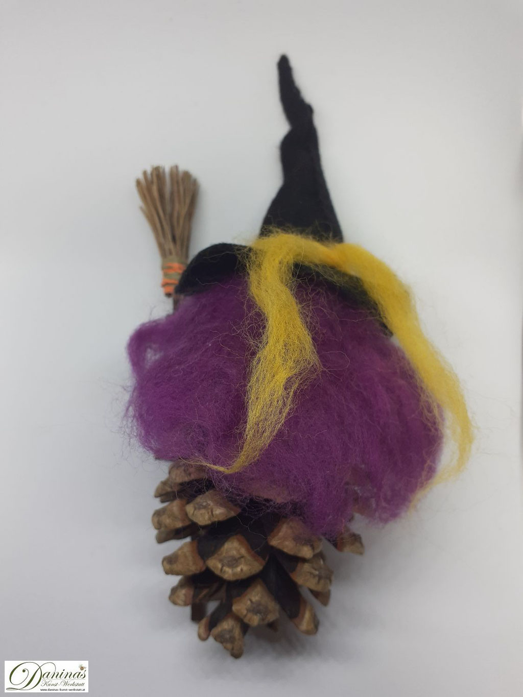 Hexe Gelbstein Rückseite. Handgefertigte Hexenfigur aus Kiefernzapfen, mit violetten langen Haaren aus Wolle und schwarzem Hexenhut, Hexenbesen aus Kiefernnadeln