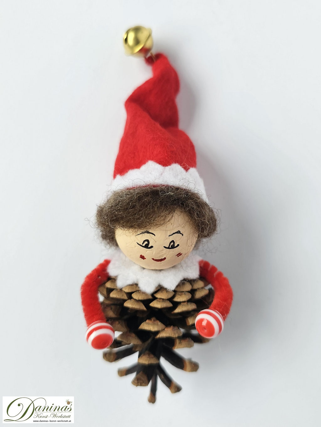 Weihnachtswichtel Floki. Handgemachte Märchenfigur aus Kiefernzapfen mit braunen Haaren aus Wolle, rot-weißer Filz-Zipfelmütze mit goldfarbigem Glöckchen, weißem Filz Kragen