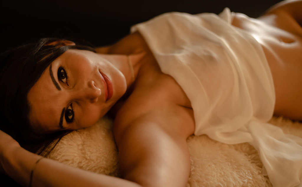 Hübsche nackte Frau liegt nur mit einem Tuch verhüllt am Boden des Fotostudio und schaut beim Aktshooting in die Kamera des Fotografen