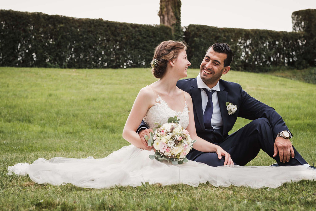 Hochzeitsfotografie eines Brautpaares sitzend auf einer Wiese.