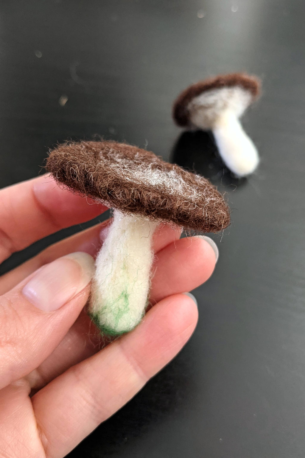 Hand holding a needle-felted mushrooms and one in the background