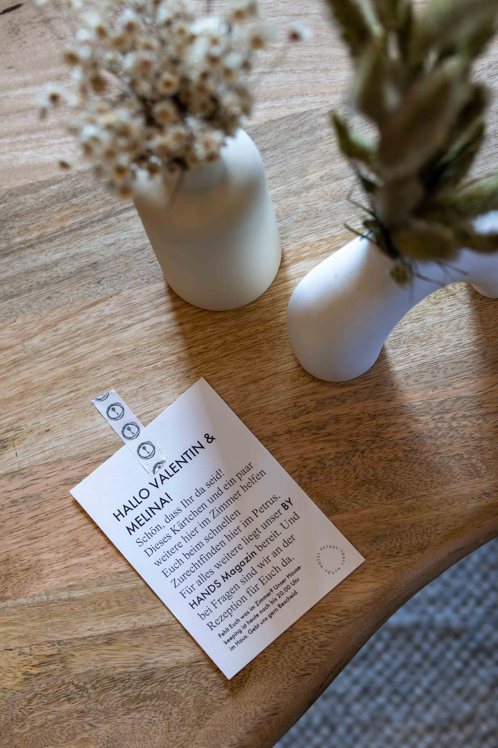 Persönliche Willkommenskarte und dezente Blumendekoration auf einem Holztisch im Boutiquehotel PETRUS in Reischach-Bruneck • Südtirol, die den herzlichen Empfang und die liebevolle Gastfreundschaft unterstreichen.