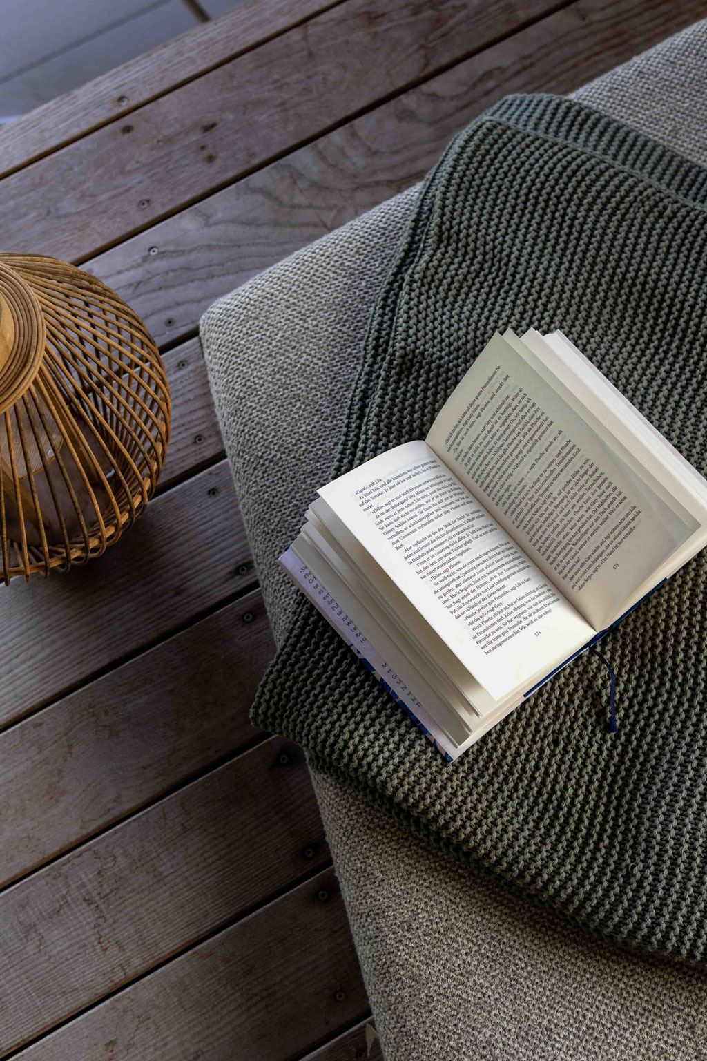 Offenes Buch auf einer weichen Strickdecke neben einer dekorativen Laterne im Wellnessbereich des Boutiquehotel PETRUS in Reischach-Bruneck • Südtirol, geschaffen für entspannte Lesemomente und erholsame Auszeiten.
