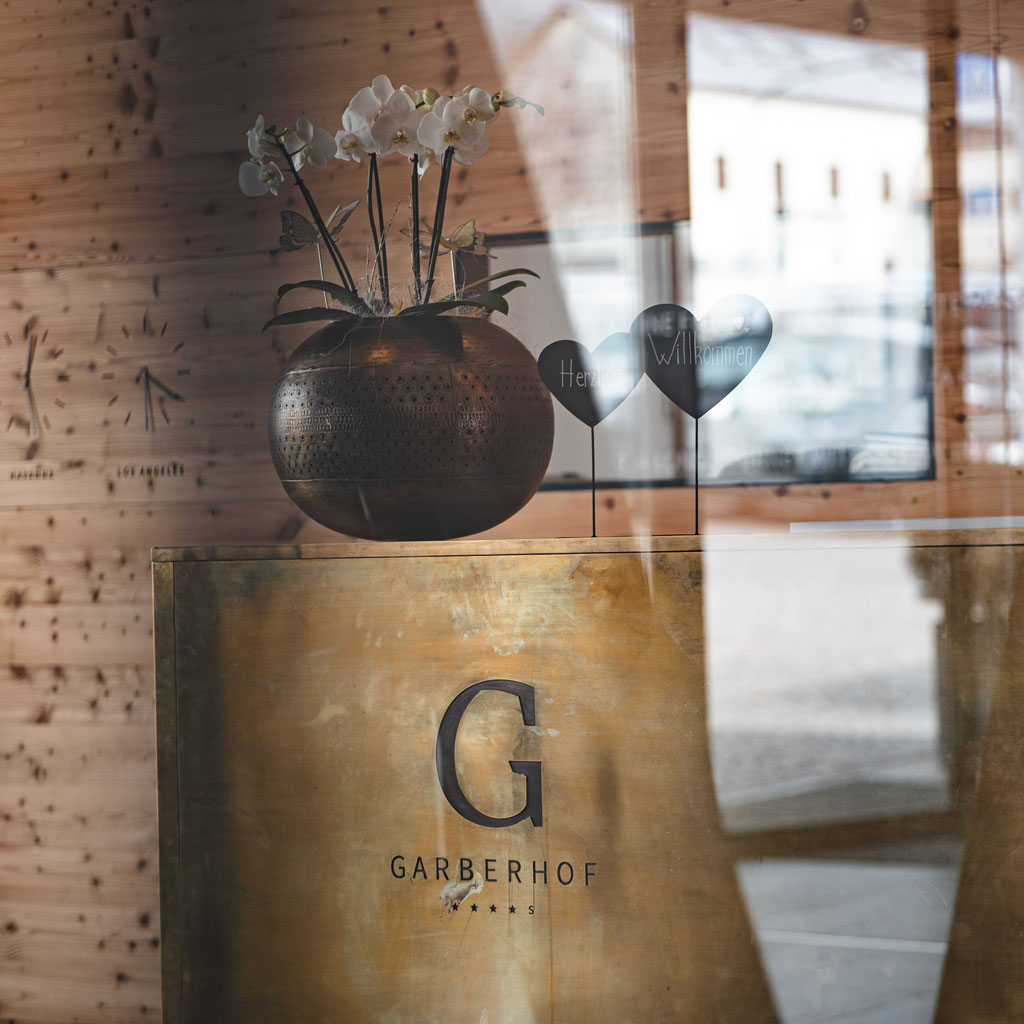 The reception area at the Garberhof, featuring a gold-coloured reception desk, an orchid arrangement and warm wooden elements.