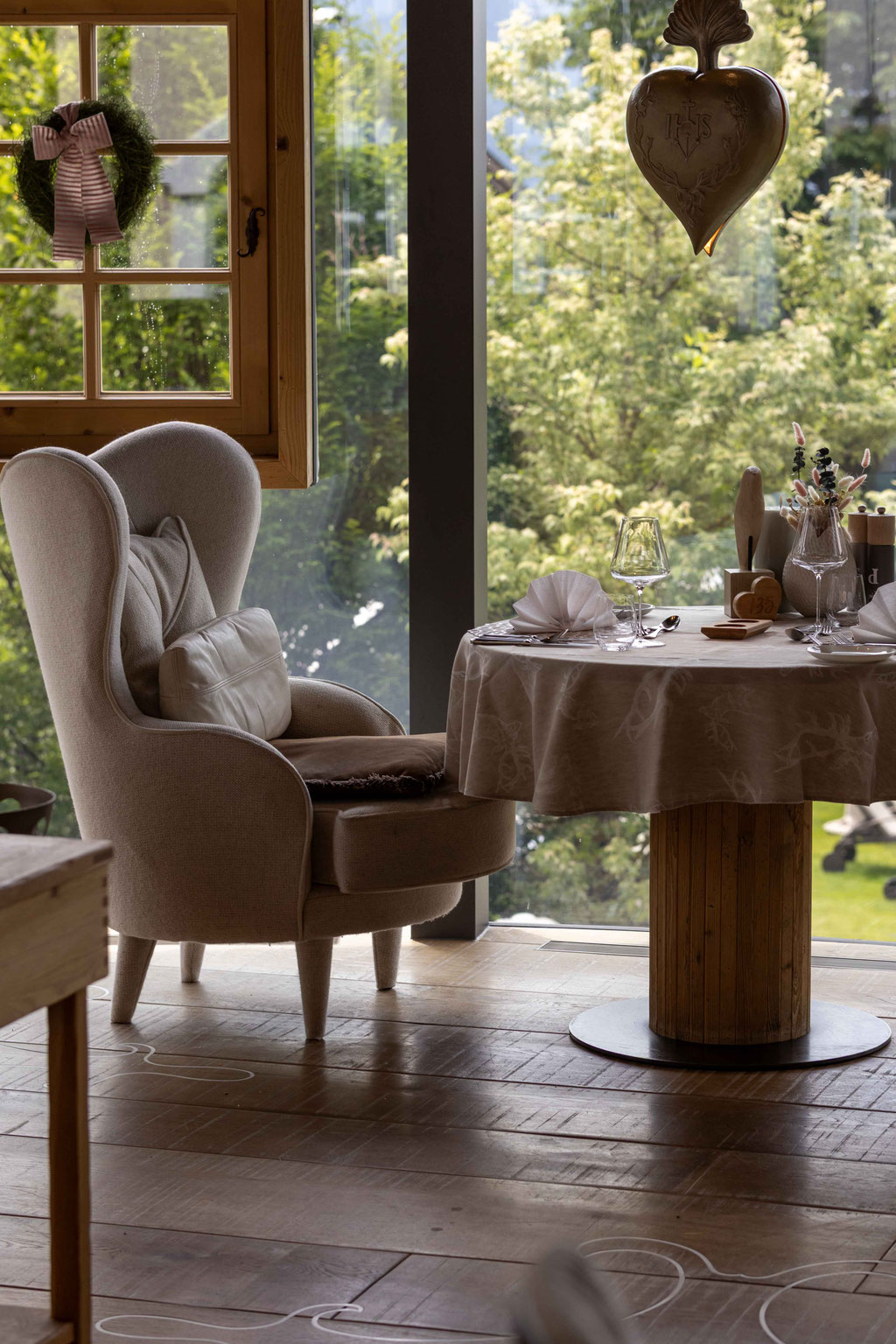 Liebevoll gedeckter Tisch am Fenster im Restaurant des DER ENGEL im Tannheimertal. Ein gemütlicher Ohrensessel, natürliche Holzelemente und der Blick ins Grüne schaffen eine ruhige, stilvolle Atmosphäre für genussvolle Momente und besondere kulinarische E