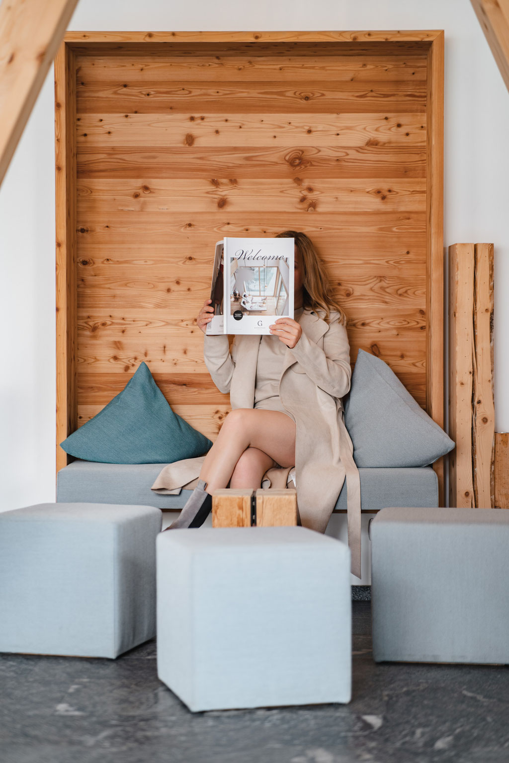 A woman is sitting in a cosy wooden alcove at the Garberhof, leisurely leafing through a hotel magazine.