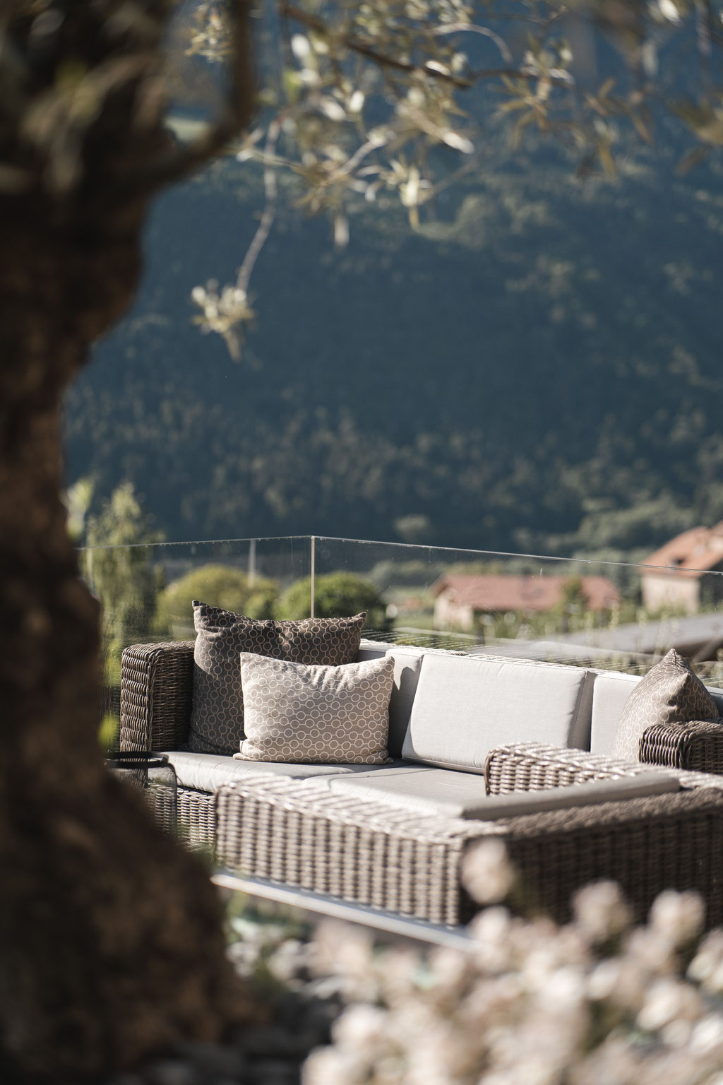 Gemütliche Outdoor-Lounge mit bequemen Rattanmöbeln und Blick auf die umliegende Berglandschaft im Hotel Mair am Ort Living in Partschins bei Meran in Südtirol. Die ruhige Gartenatmosphäre lädt zum Entspannen und Verweilen im Freien ein.