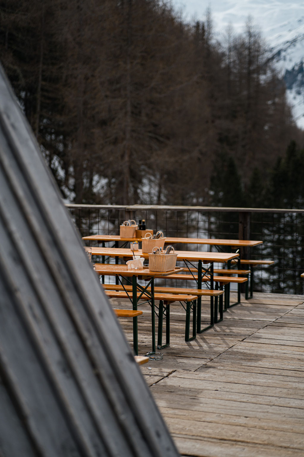 Holzterrasse mit Bierbänken vor winterlichem Waldpanorama.