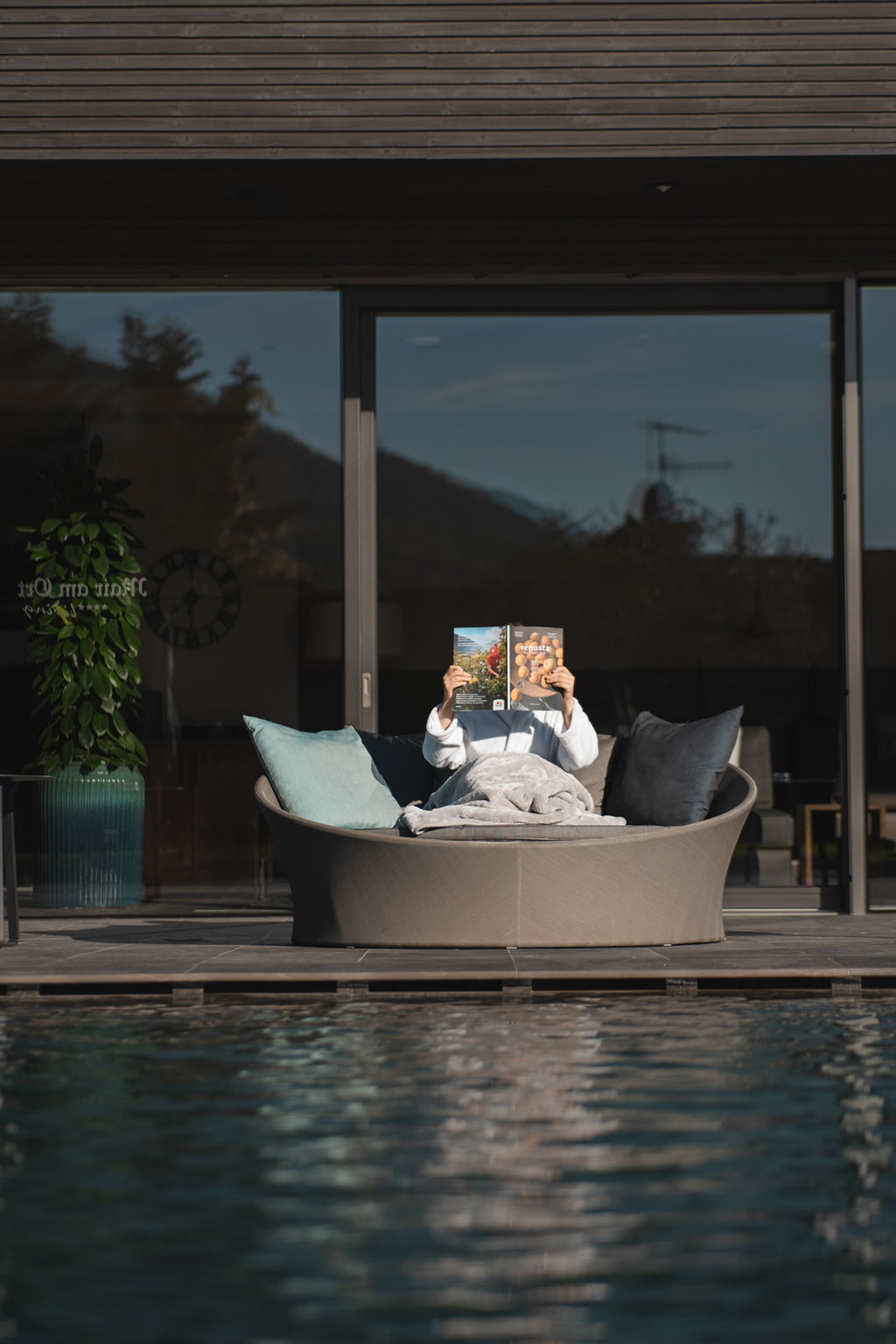 Gast entspannt mit einer Zeitschrift auf einer gemütlichen Loungeinsel am Pool des Hotel Mair am Ort Living in Partschins bei Meran in Südtirol. Der moderne Außenbereich mit Pool und Terrasse schafft eine ruhige Atmosphäre zum Lesen und Erholen.