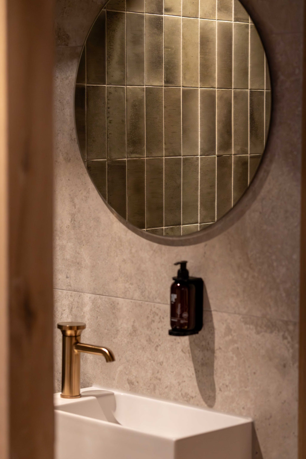 Edles Waschbecken mit goldfarbener Armatur und rundem Spiegel im stilvollen Badezimmer des DER ENGEL im Tannheimertal. Hochwertige Materialien, warme Lichtstimmung und modernes Design schaffen eine elegante Wohlfühlatmosphäre.