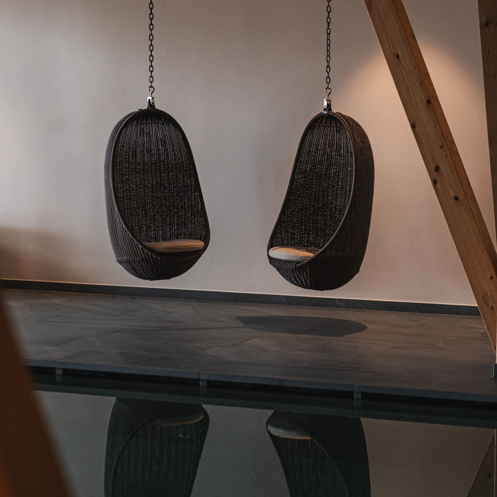 Zwei hängende Loungesessel im Spa-Bereich des Garberhof über einem ruhigen Wasserbecken.